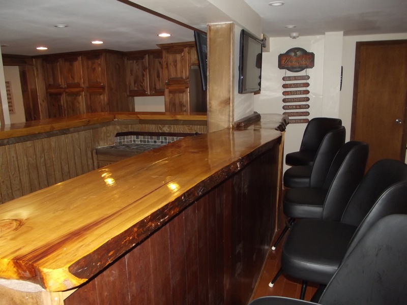 A bar in a home with black chairs and a tv.