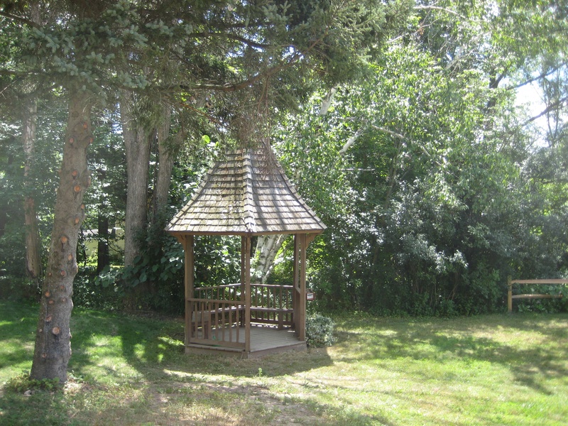 A wooden gazebo in the middle of a grassy area.