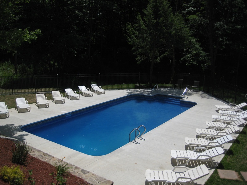 A swimming pool with white chairs and a fence.
