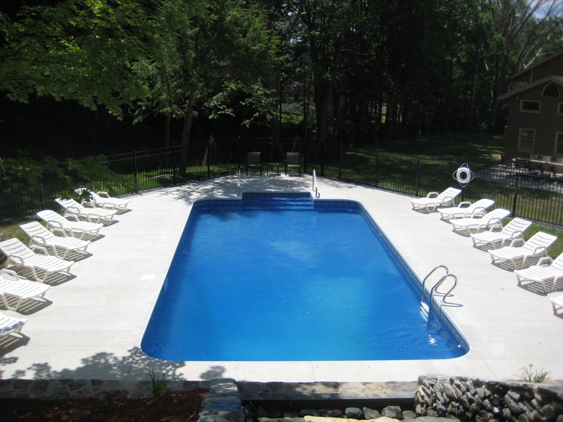 A swimming pool in a backyard with chairs around it.