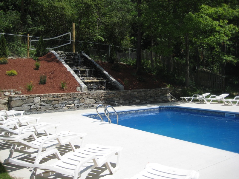 A swimming pool with white chairs and a stone wall.