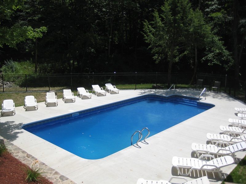 A swimming pool with chairs and a tree in the background.