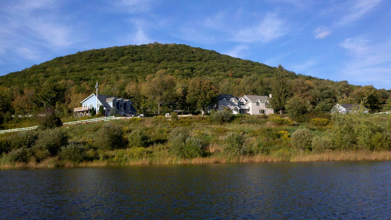 A house sits on top of a hill next to a lake.