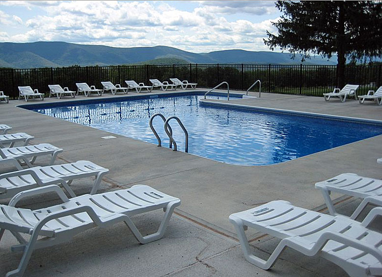 A swimming pool with white chairs and a view of mountains.