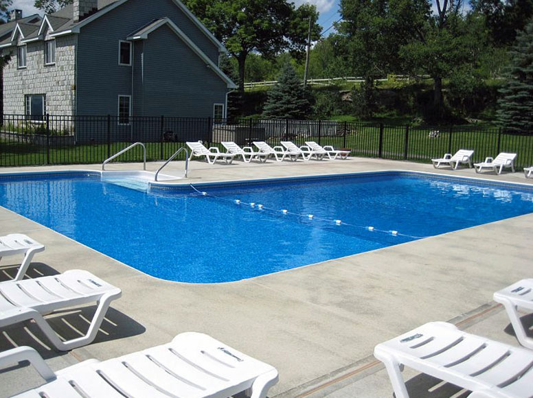 A swimming pool with white chairs and a house in the background.