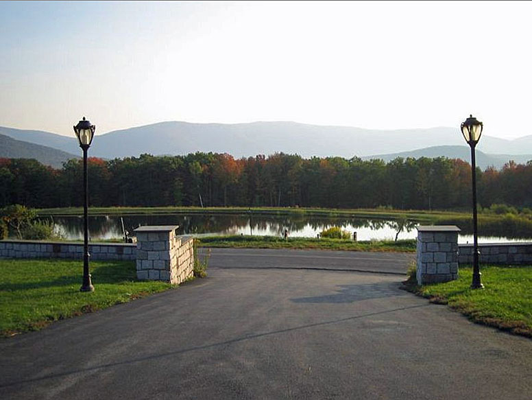 A driveway leading to a pond and mountains.