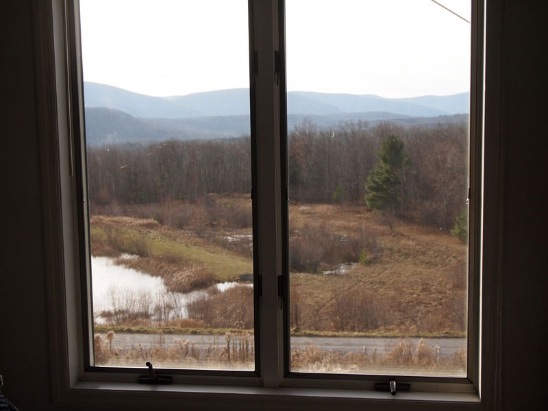 A window with a view of a field and mountains.