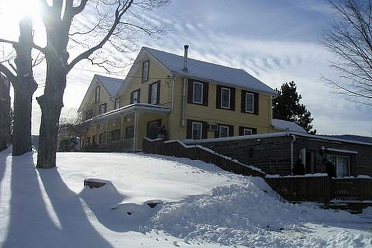 A yellow house is covered in snow on the side of a hill.