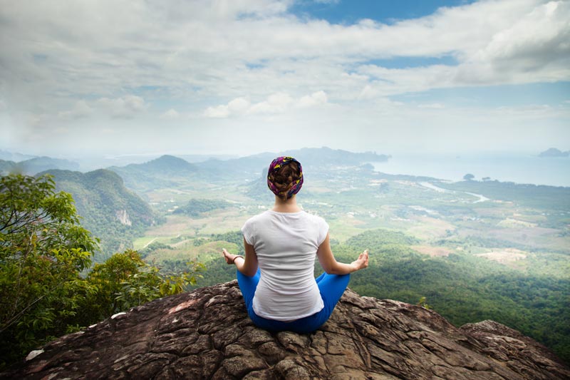 A woman is meditating on top of a mountain.