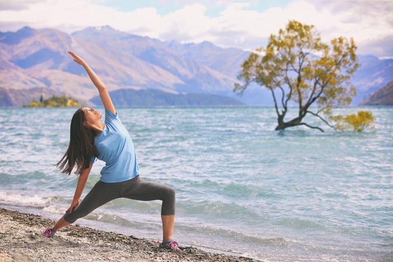 A woman practicing yoga on the shore of lake wanaka.