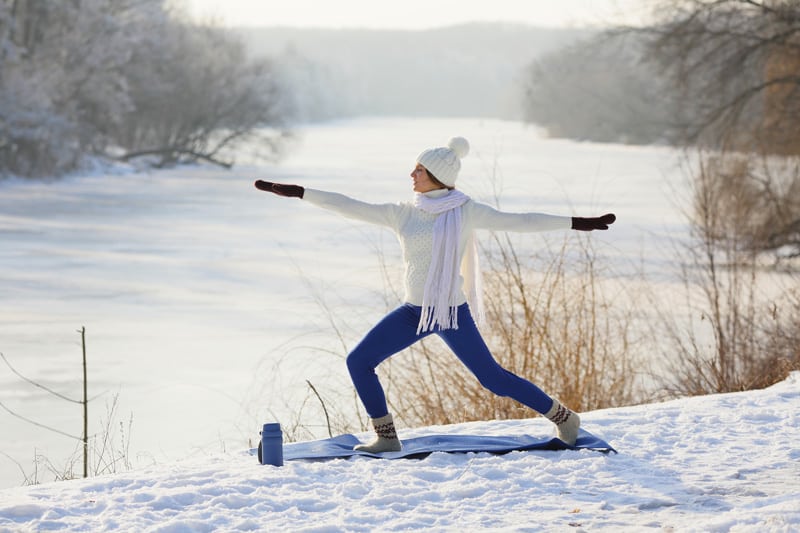A woman is doing yoga on a snow board near a river.