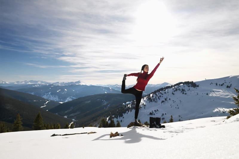 A woman practicing yoga on top of a snowy mountain.