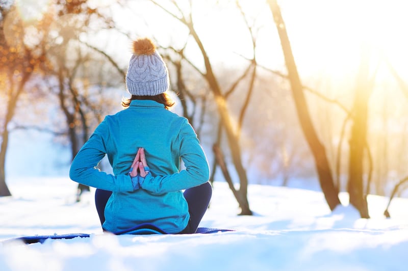 A woman is sitting in the snow doing yoga.