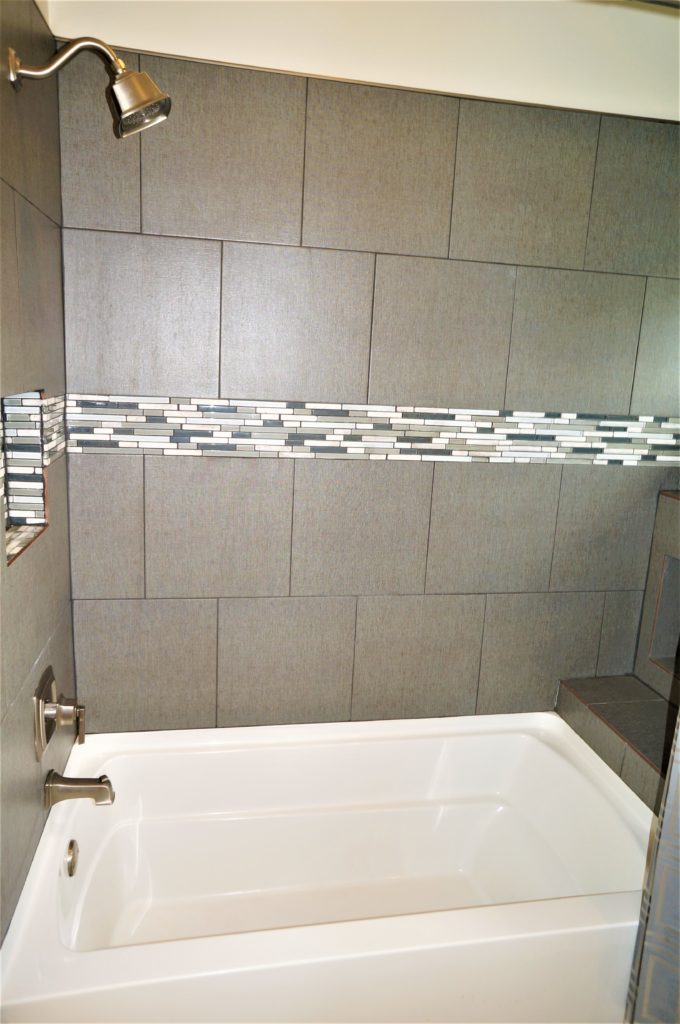 A bathtub in a bathroom with tiled walls.