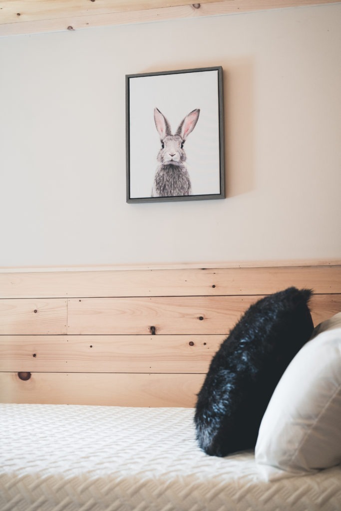 A bedroom with a bunny on the wall above a bed.