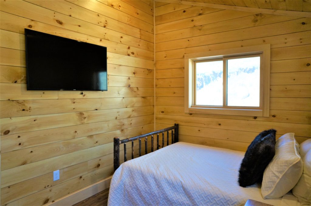 A bed in a cabin with a tv above it.