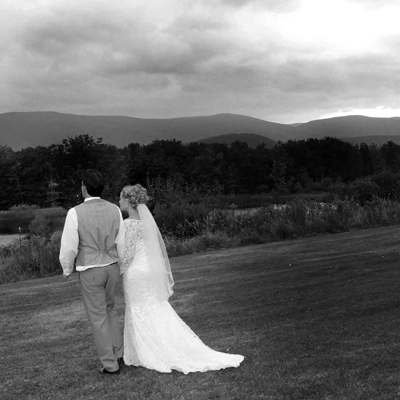 A bride and groom walking in a field with mountains in the background.