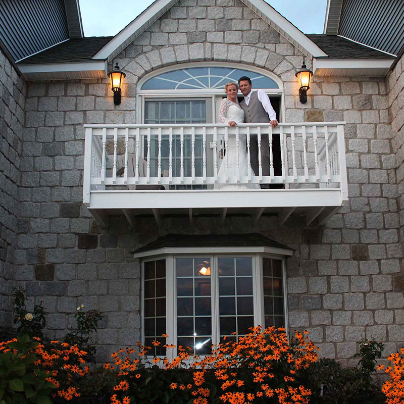 A bride and groom standing on the balcony of a house.