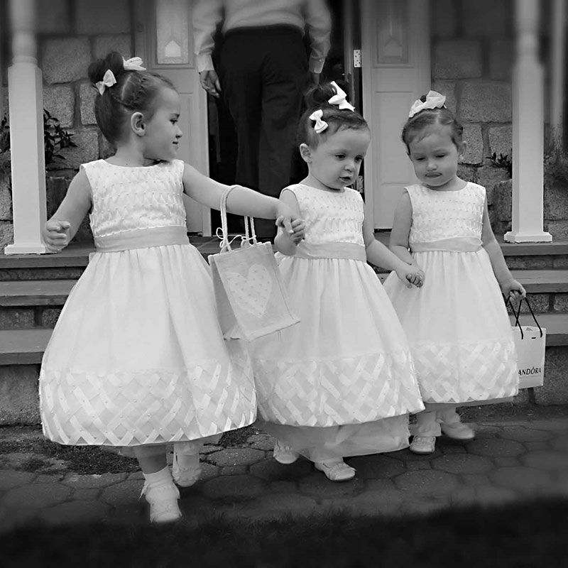 Three little girls in white dresses standing in front of a door.