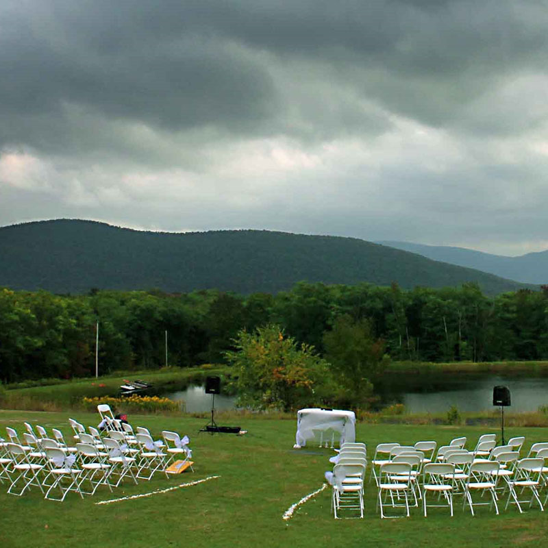 A field with white chairs set up for a wedding ceremony.