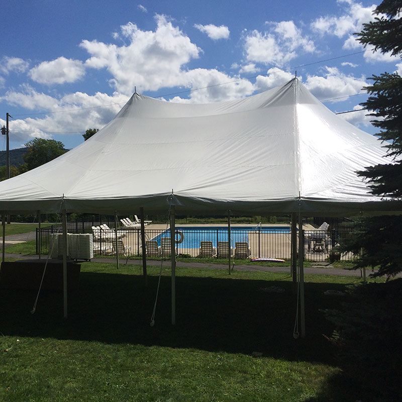 A white tent set up in a grassy area near a swimming pool.