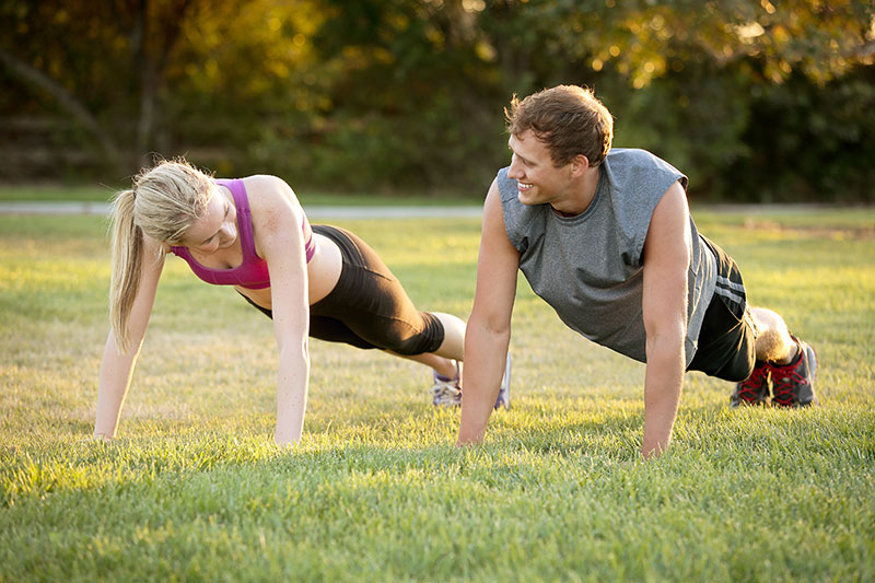 A man and woman doing push ups in the grass.