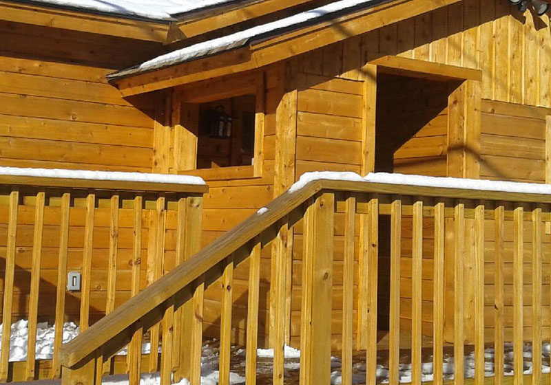 A wooden cabin in the snow with a wooden deck.