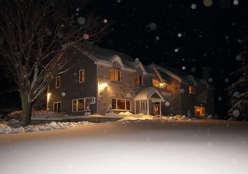 A house is lit up at night with snow falling around it.