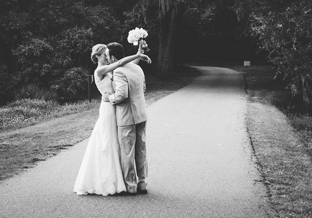 Black and white photo of bride and groom hugging on a path.