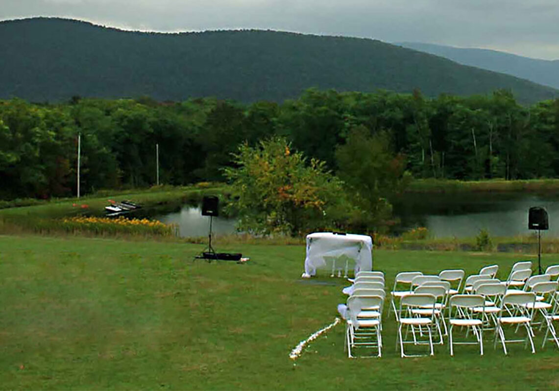 A wedding ceremony set up on a grassy field with mountains in the background.
